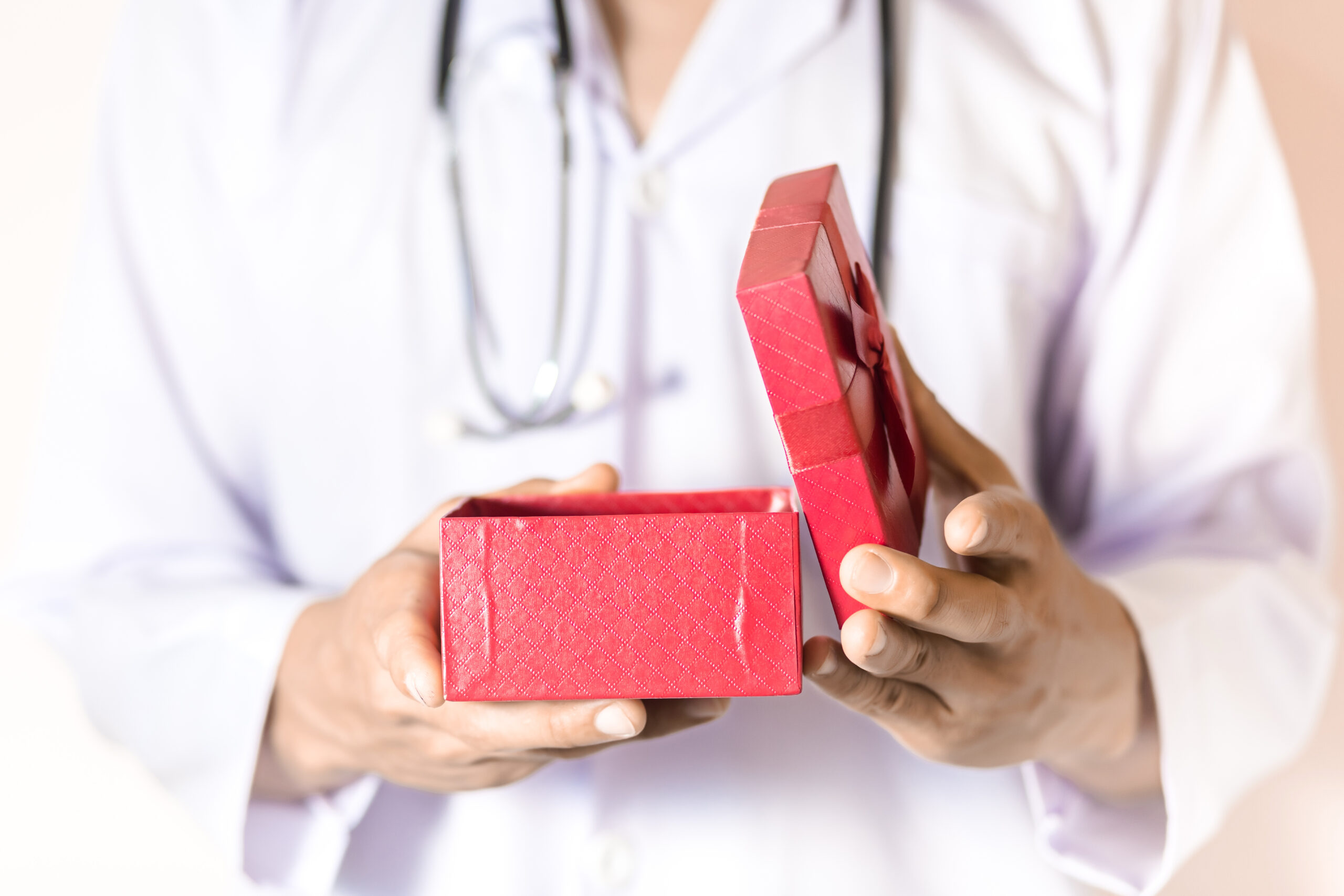 medecin tenant dans la main une boite de cadeau rouge